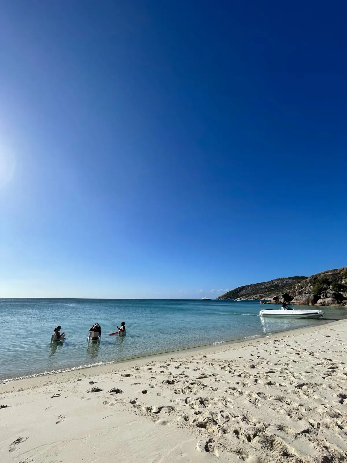 Guests sitting in chairs in the shallows of an empty Lizard Island beach, the tender pulled up on the sand