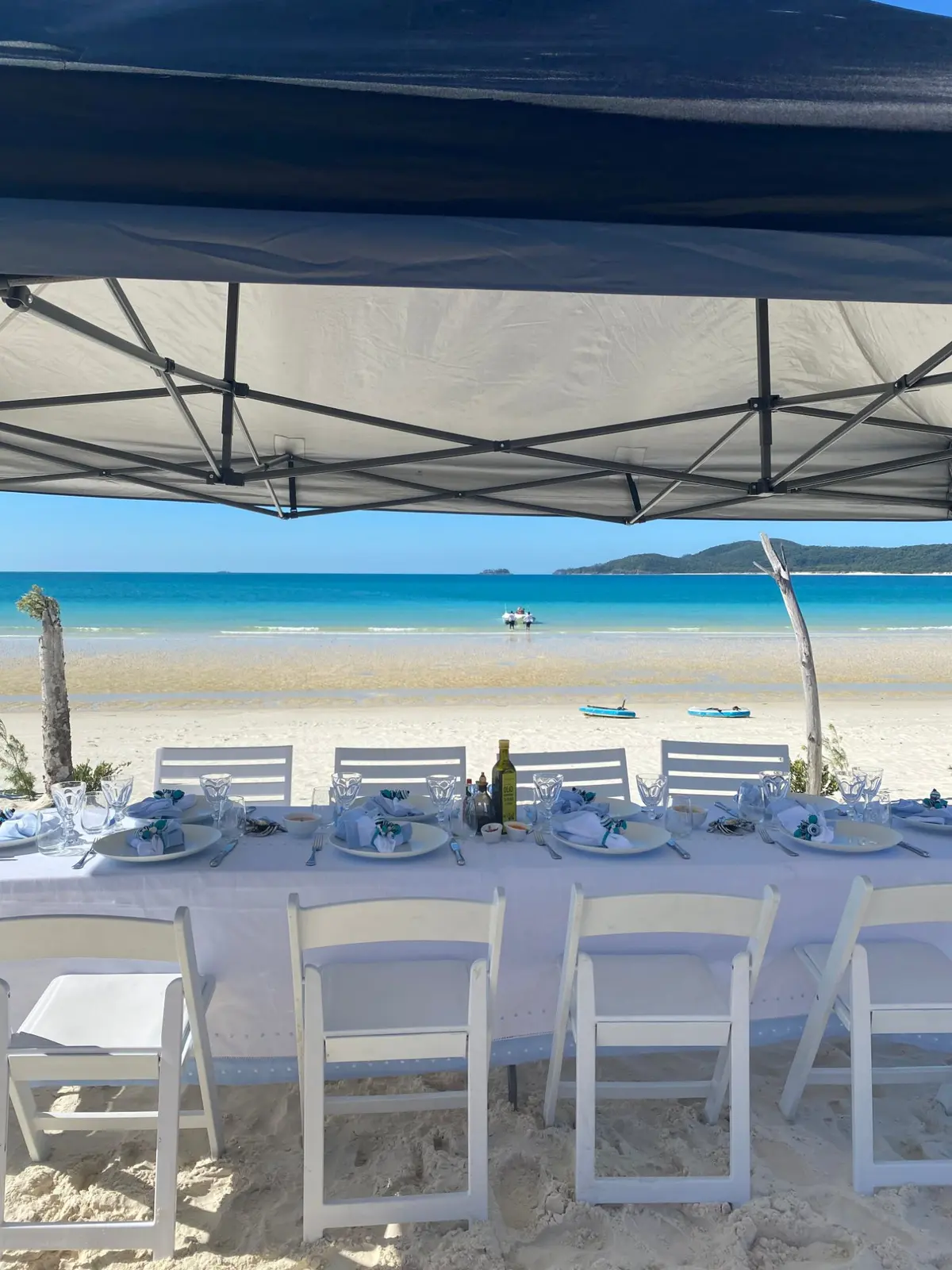 A long table set for lunch on a white-sand beach in the Whitsundays, the tender landing guests in the shallows