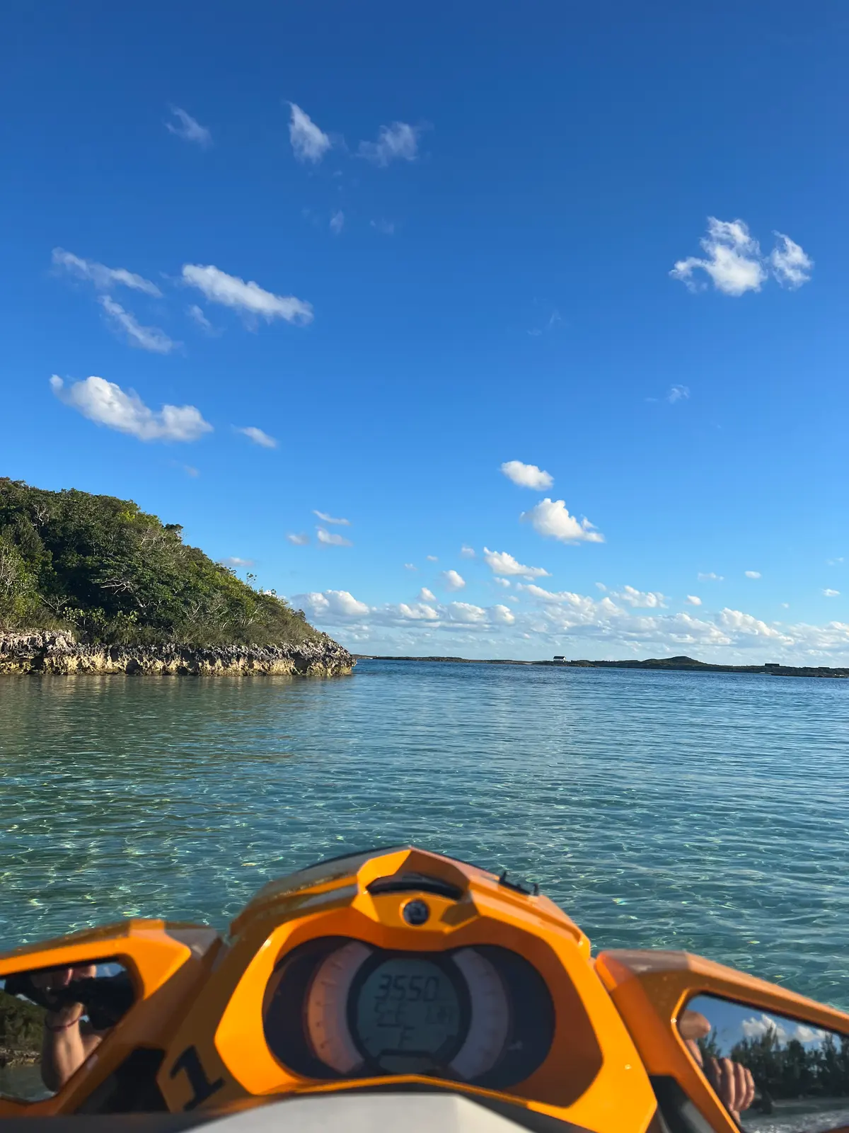 Over the handlebars of a jet ski, flat water and a rocky cay