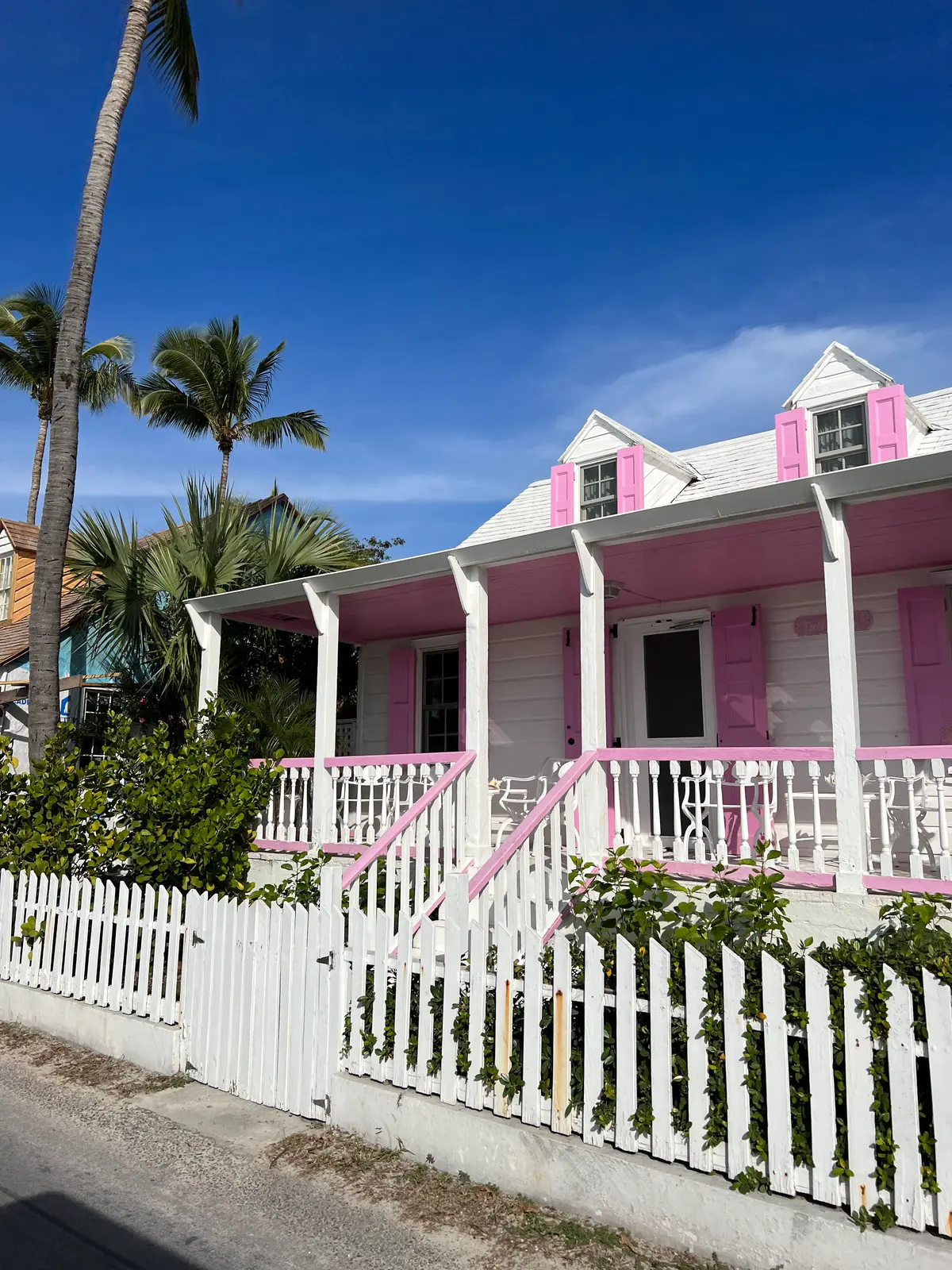 A white cottage with pink shutters and a picket fence in Dunmore Town