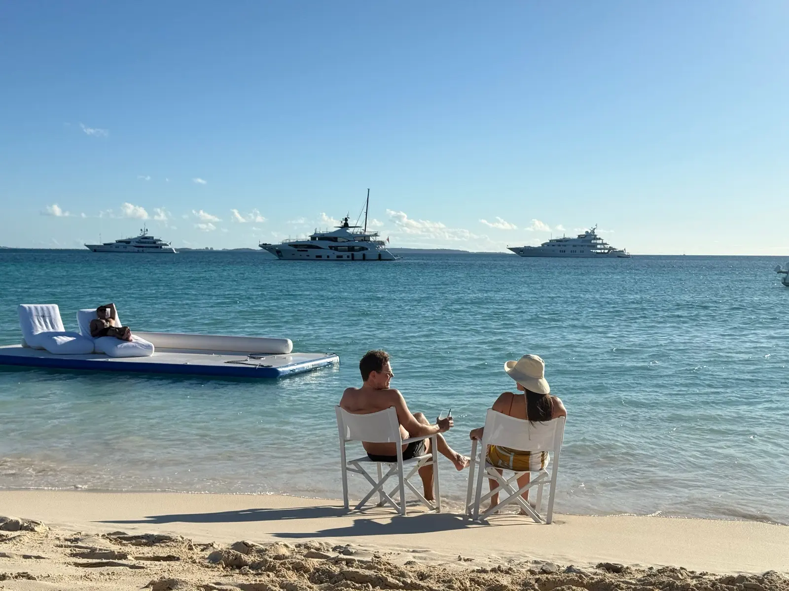 Two deck chairs at the water's edge in Anguilla, the yachts at anchor