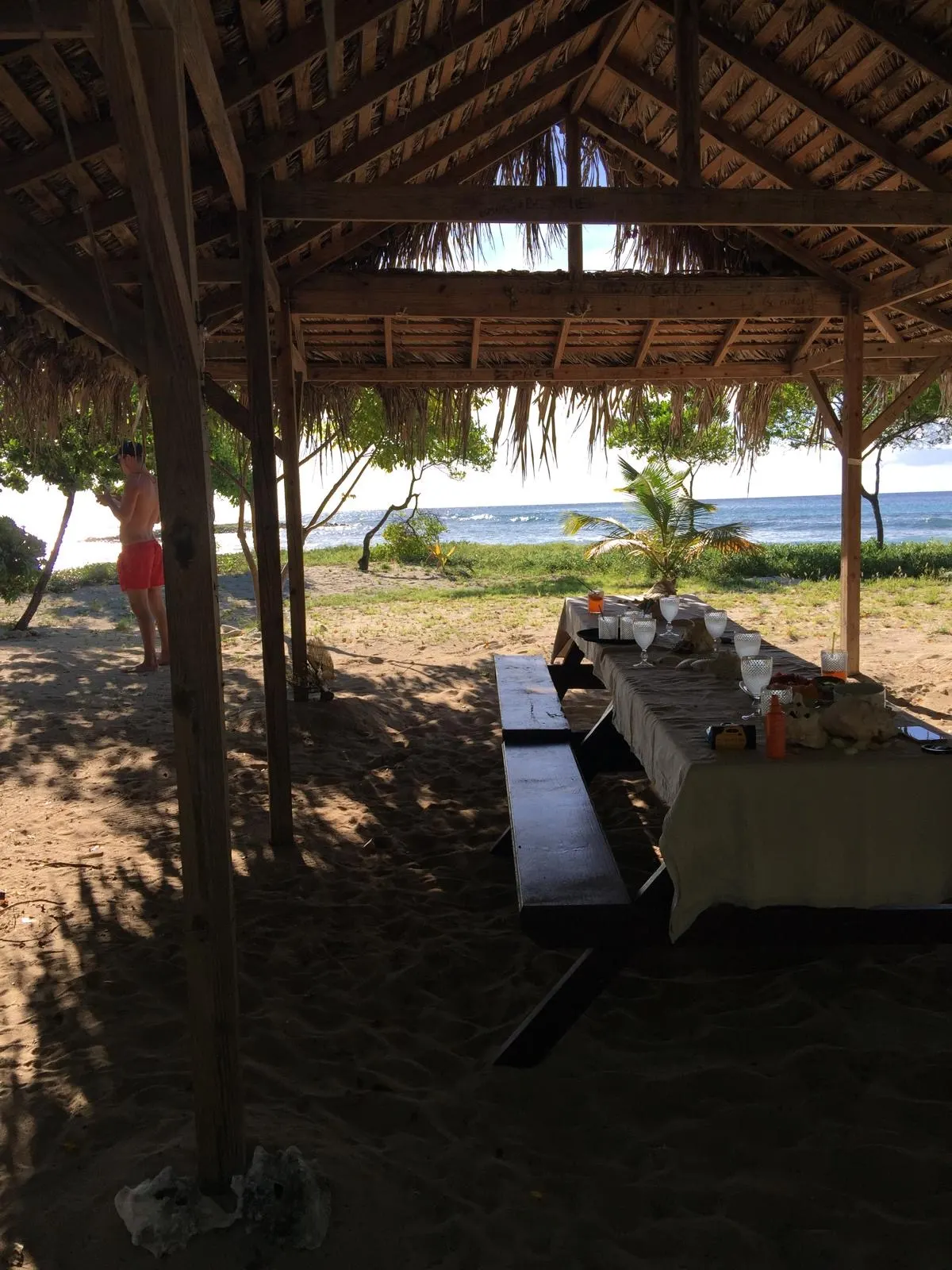 The picnic table laid under a thatched hut on the beach in Mustique, the sea behind