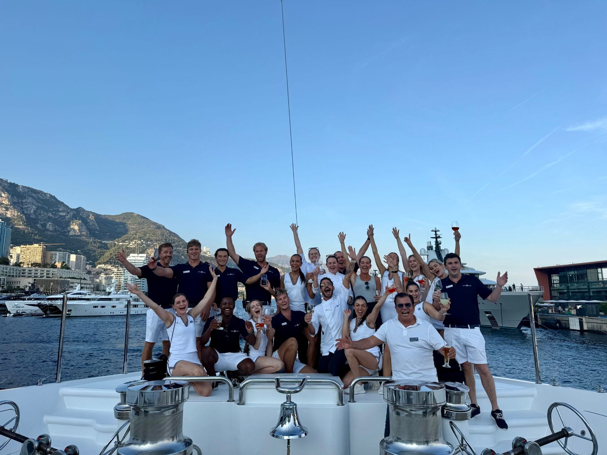 The Ahoy Club team celebrating on the foredeck of a yacht in Port Hercules during Monaco Yacht Show 2026