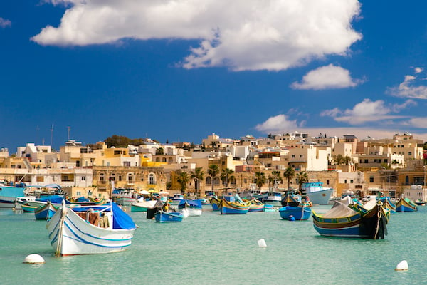 Colorful, traditional fishing boats against the backdrop of Marsaxlokk village in the mediterranean island of Malta