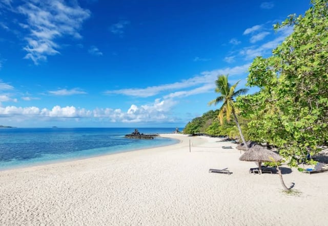 Beautiful beach with palm trees lounge chairs, beach volleyball net and beach huts in Mamanuca Islands, Fiji