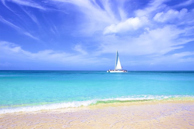Small sailboat under big white clouds in Caribbean ocean 