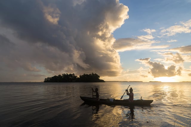 Children on the way to school with a canoe during sunrise in the Solomon Islands.